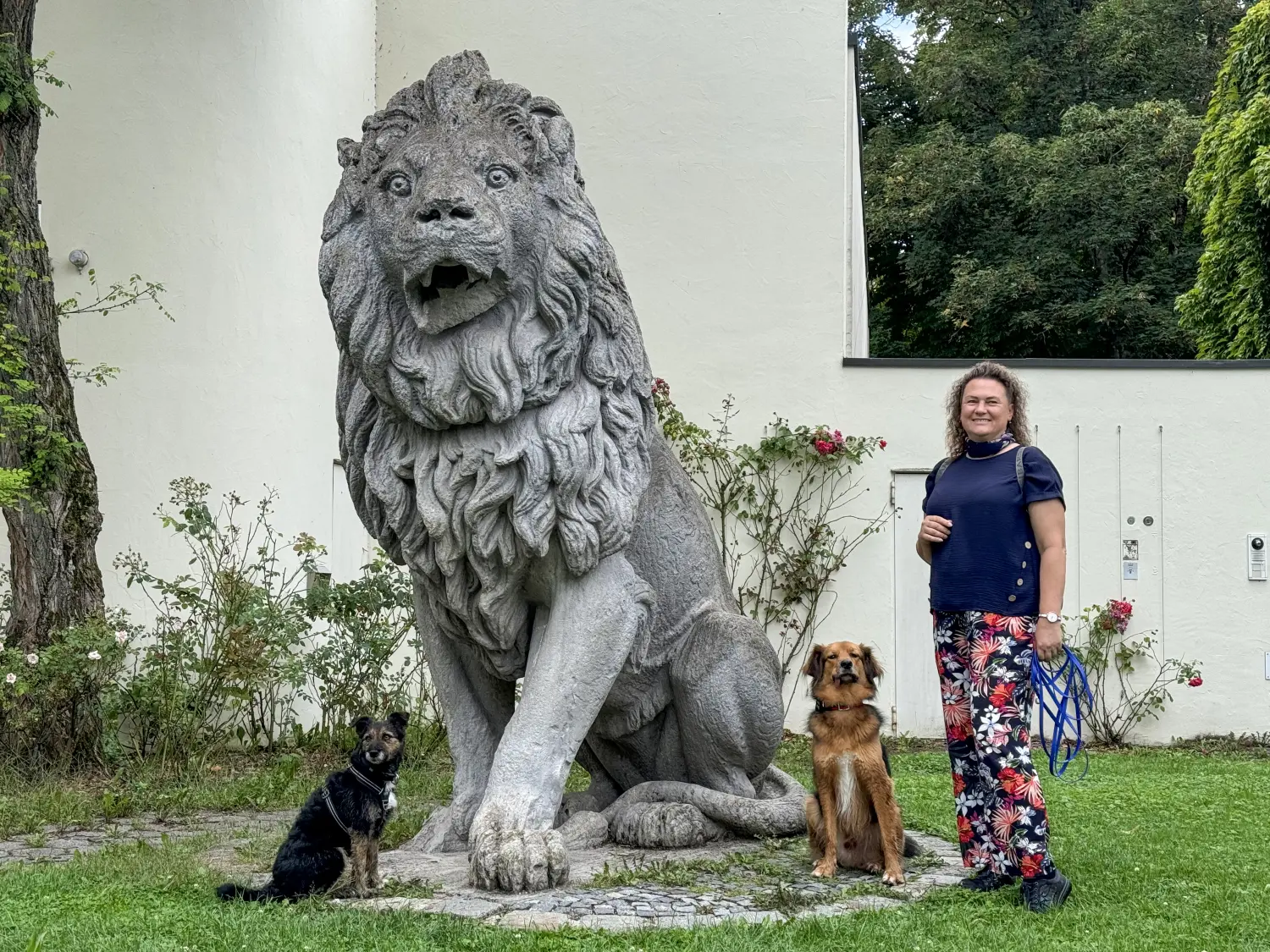 Paulchens-Hundeschule / Hunde-und Tierfotografie - Hundetraining und Fotografie - Claudia Willing mit zwei Hunden neben einer großen, reich verzierten Löwenstatue aus Stein im Freien.
